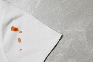 Photo of Dirty t-shirt with stains of sauce on light grey marble table, top view. Space for text