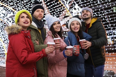 Happy friends with cups of mulled wine at winter fair