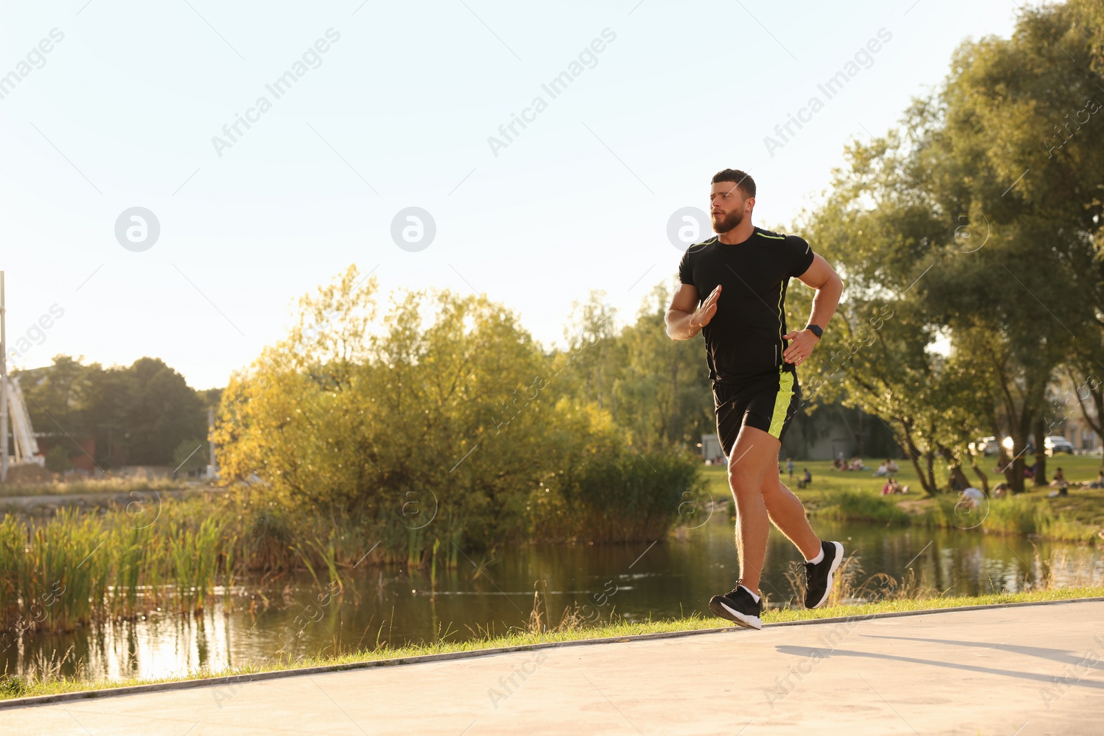 Photo of Young man running near pond in park. Space for text