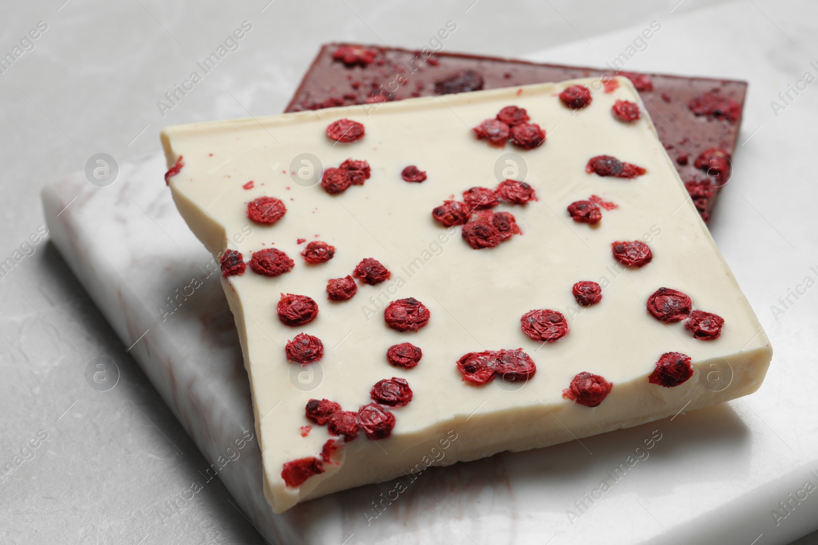 Photo of Board and different chocolate bars with freeze dried fruits on light marble table, closeup