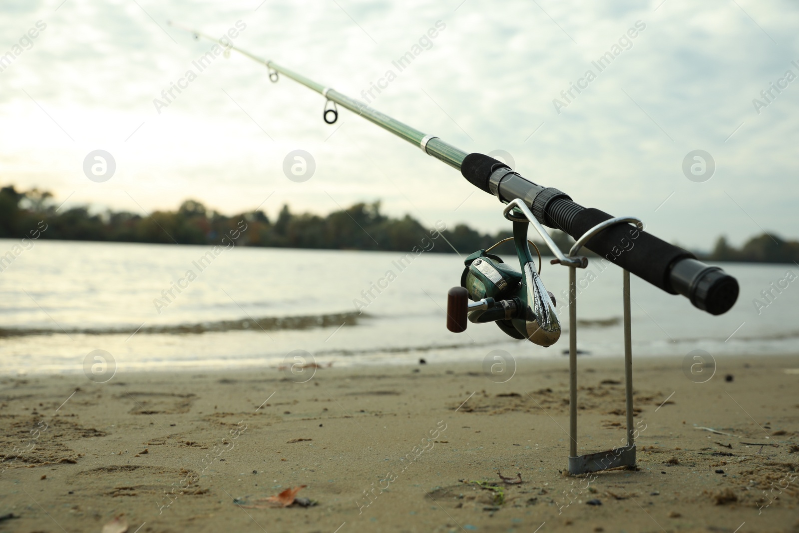 Photo of Fishing rod with reel on sand near river, space for text