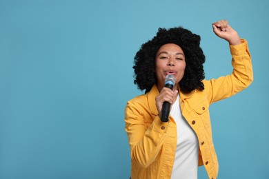 Beautiful woman with microphone singing on light blue background, space for text