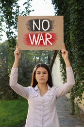 Photo of Sad woman holding poster with words No War outdoors