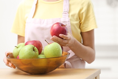 Woman with bowl of fresh apples at table in kitchen, closeup