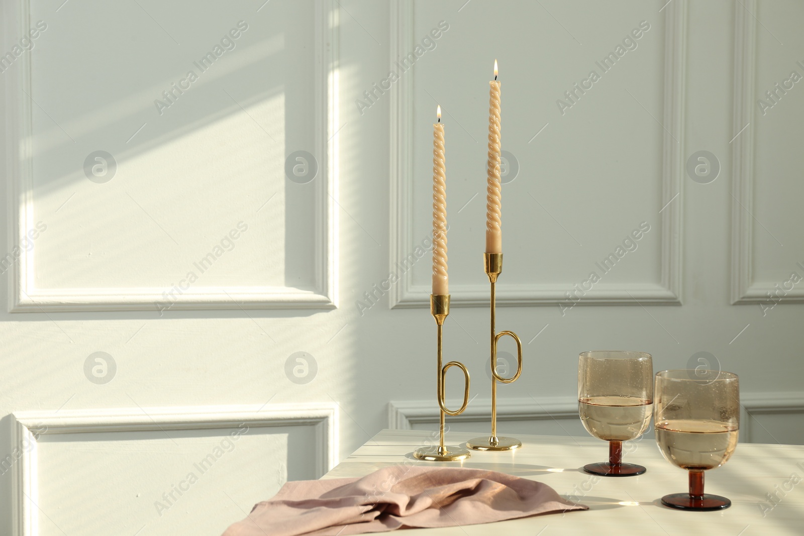 Photo of Glasses of wine near burning candles on white table indoors, space for text