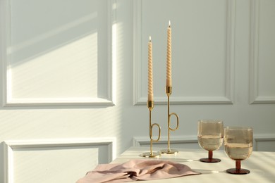Photo of Glasses of wine near burning candles on white table indoors, space for text