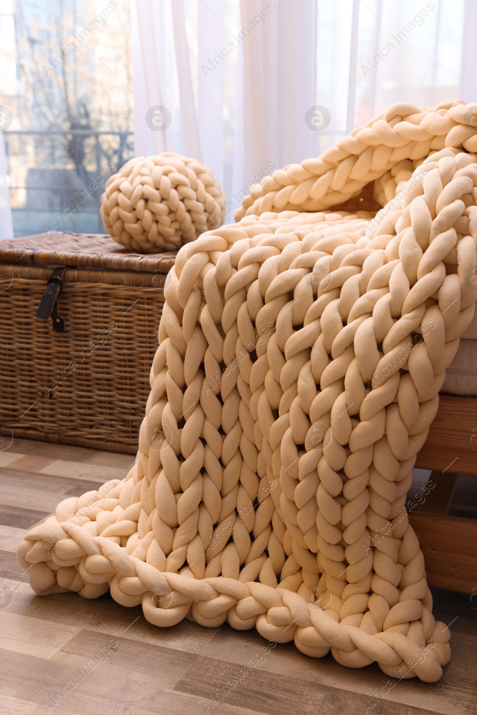 Photo of Beautiful knitted blanket and pillow near window in room