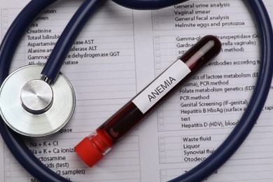 Test tube with blood sample and stethoscope on medical form, flat lay. Anemia concept