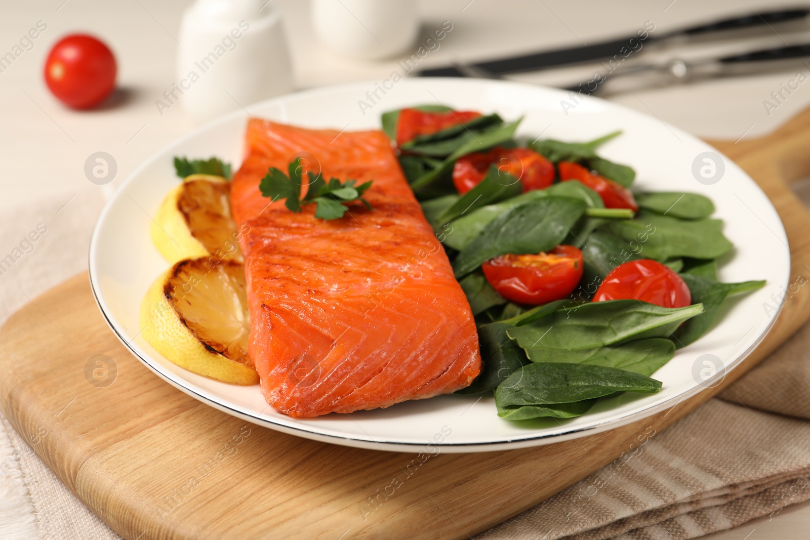 Photo of Tasty grilled salmon with basil, tomatoes and lemon on table, closeup