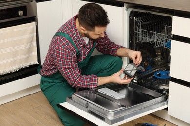 Photo of Repairman holding drain filter near dishwasher in kitchen