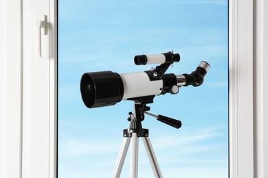 Tripod with modern telescope near window indoors, closeup