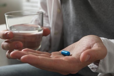 Man with glass of water and pill on blurred background, closeup