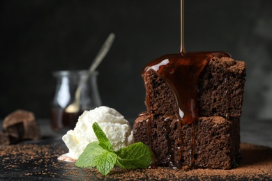Photo of Pouring sauce onto fresh brownies served with ice-cream on slate plate, space for text. Delicious chocolate pie