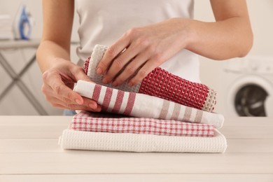 Woman with clean kitchen towels at white wooden table in laundry room, closeup