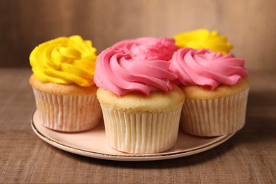 Photo of Delicious cupcakes with bright cream on wooden table, closeup