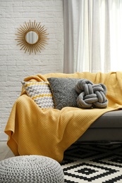 Photo of Soft pillows and yellow plaid on sofa in living room