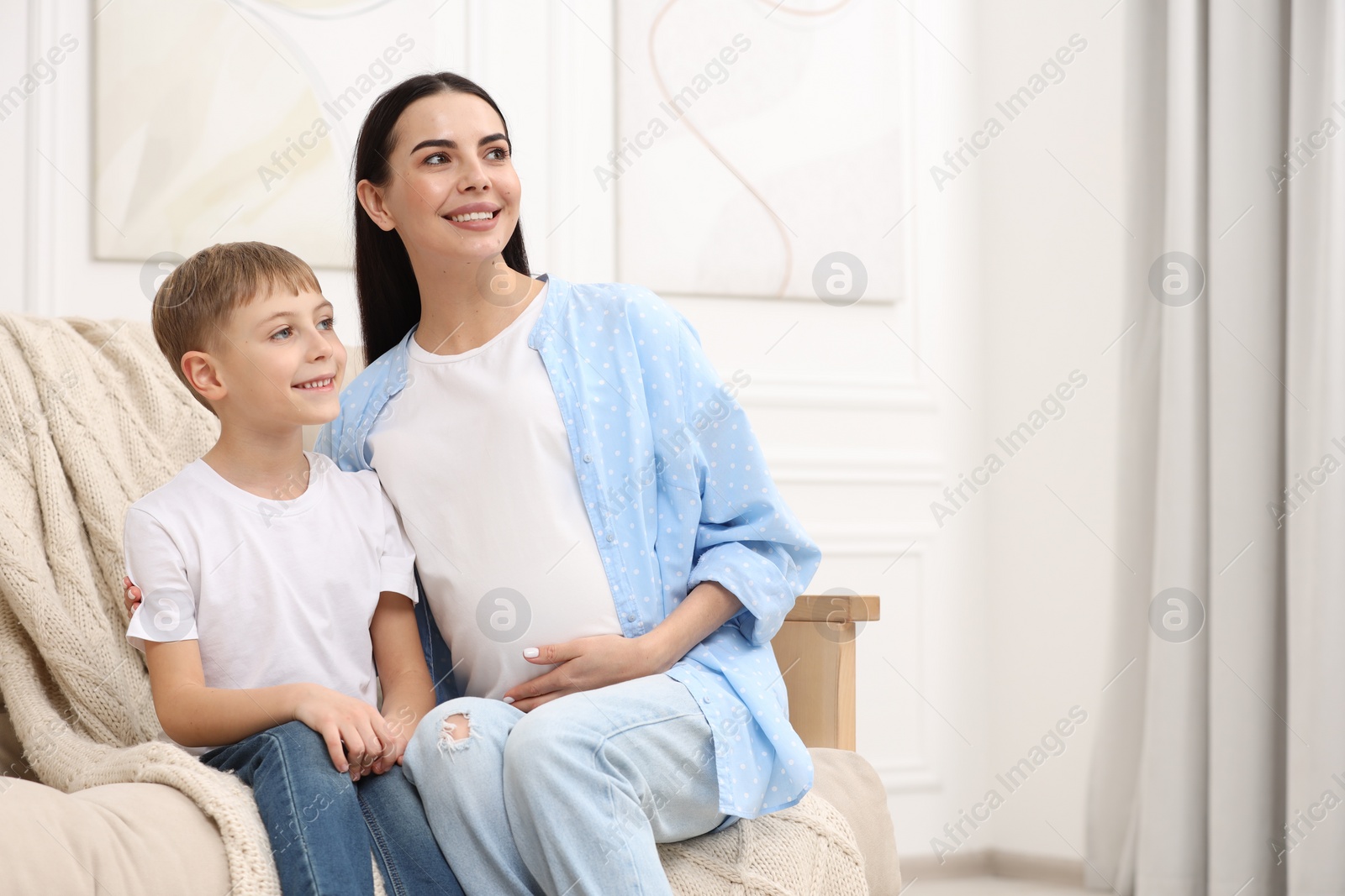 Photo of Happy pregnant woman with her son on sofa at home, space for text