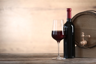 Glass and bottle of red wine near wooden barrel on table. Space for text