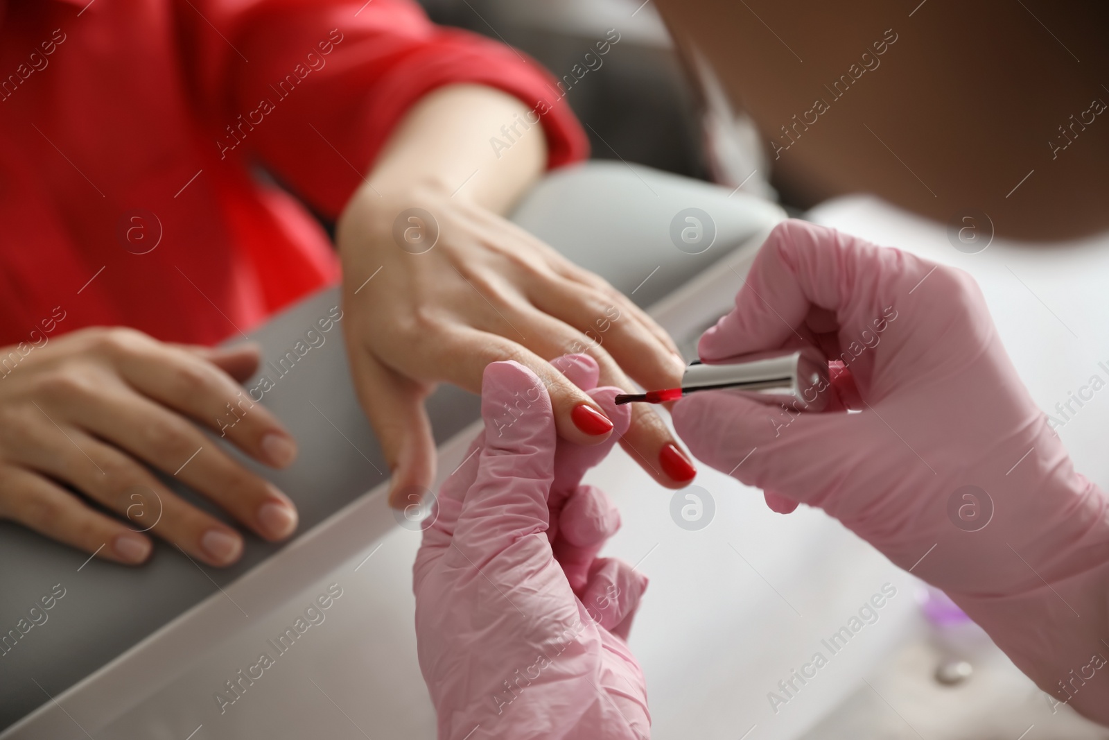 Photo of Professional manicurist applying polish on client's nails in beauty salon, closeup