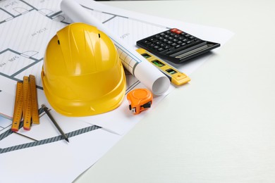 Photo of Construction drawings, safety hat, calculator, tape measure, folding ruler and bubble level on white background. Space for text