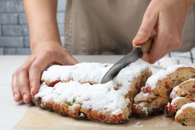 Photo of Woman cutting traditional Christmas Stollen with icing sugar at white wooden table, closeup
