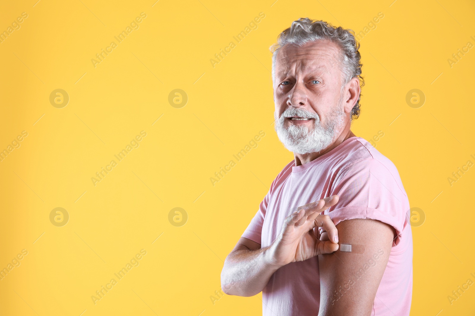 Photo of Cheerful senior man showing arm with bandage after vaccination on yellow background. Space for text