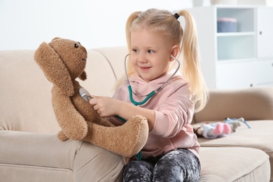 Cute child imagining herself as doctor while playing with stethoscope and toy bunny at home