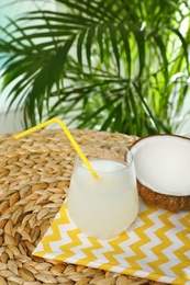 Composition with glass of coconut water on wicker table against blurred background