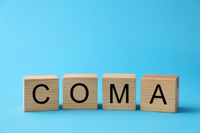 Photo of Wooden cubes with word Coma on light blue background, closeup