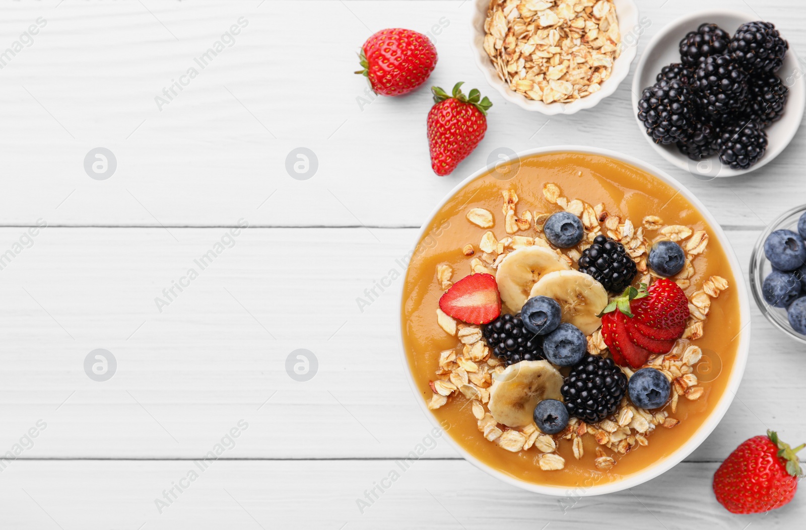 Photo of Delicious smoothie bowl with fresh berries, banana and oatmeal on white wooden table, flat lay. Space for text