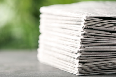 Stack of newspapers on grey table against blurred green background, closeup. Journalist's work