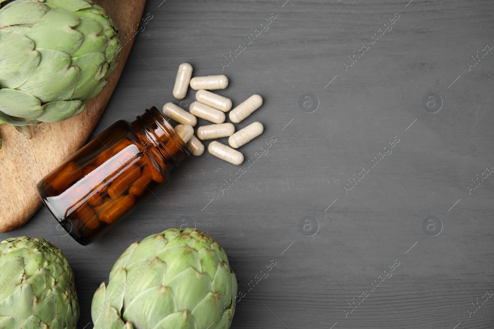 Photo of Bottle with pills and fresh artichokes on grey wooden table, flat lay. Space for text