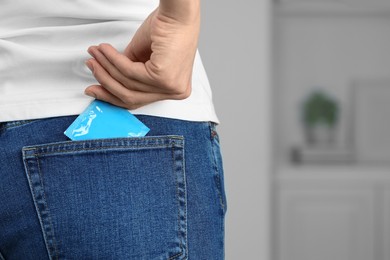 Woman pulling condom out of pocket indoors, closeup and space for text. Safe sex