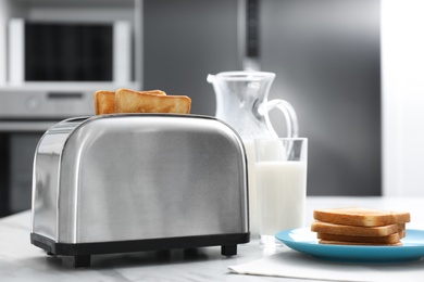 Modern toaster with slices of bread and milk on white table in kitchen