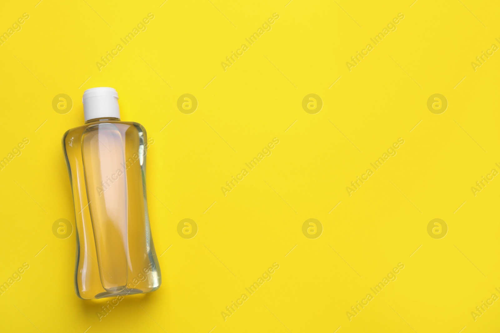Photo of Bottle of baby oil on yellow background, top view. Space for text