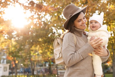 Happy mother with her baby daughter outdoors on autumn day, space for text