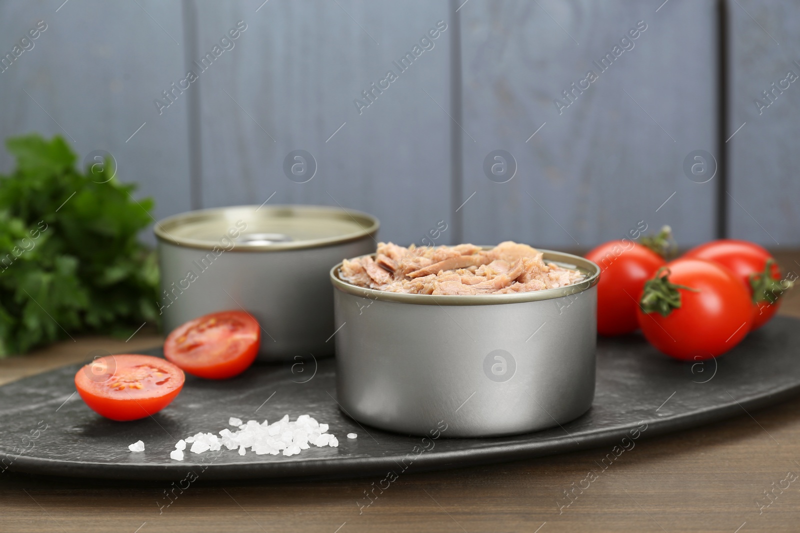 Photo of Tin cans with canned tuna and tomatoes on wooden table