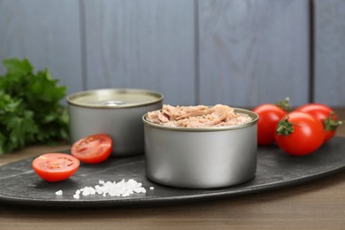 Tin cans with canned tuna and tomatoes on wooden table