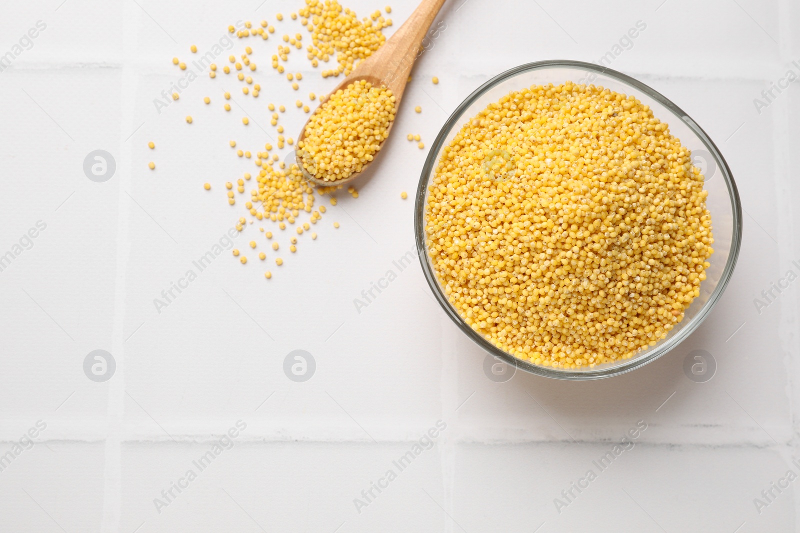 Photo of Millet groats in bowl and spoon on white tiled table, flat lay. Space for text