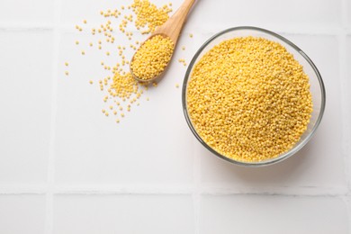 Photo of Millet groats in bowl and spoon on white tiled table, flat lay. Space for text