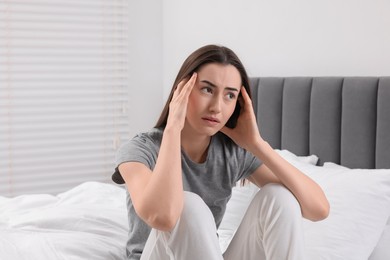 Photo of Sad woman suffering from headache on bed indoors