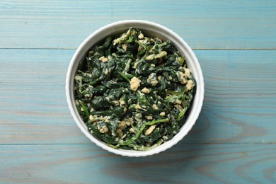 Photo of Tasty spinach dip with egg in bowl on light blue wooden table, top view