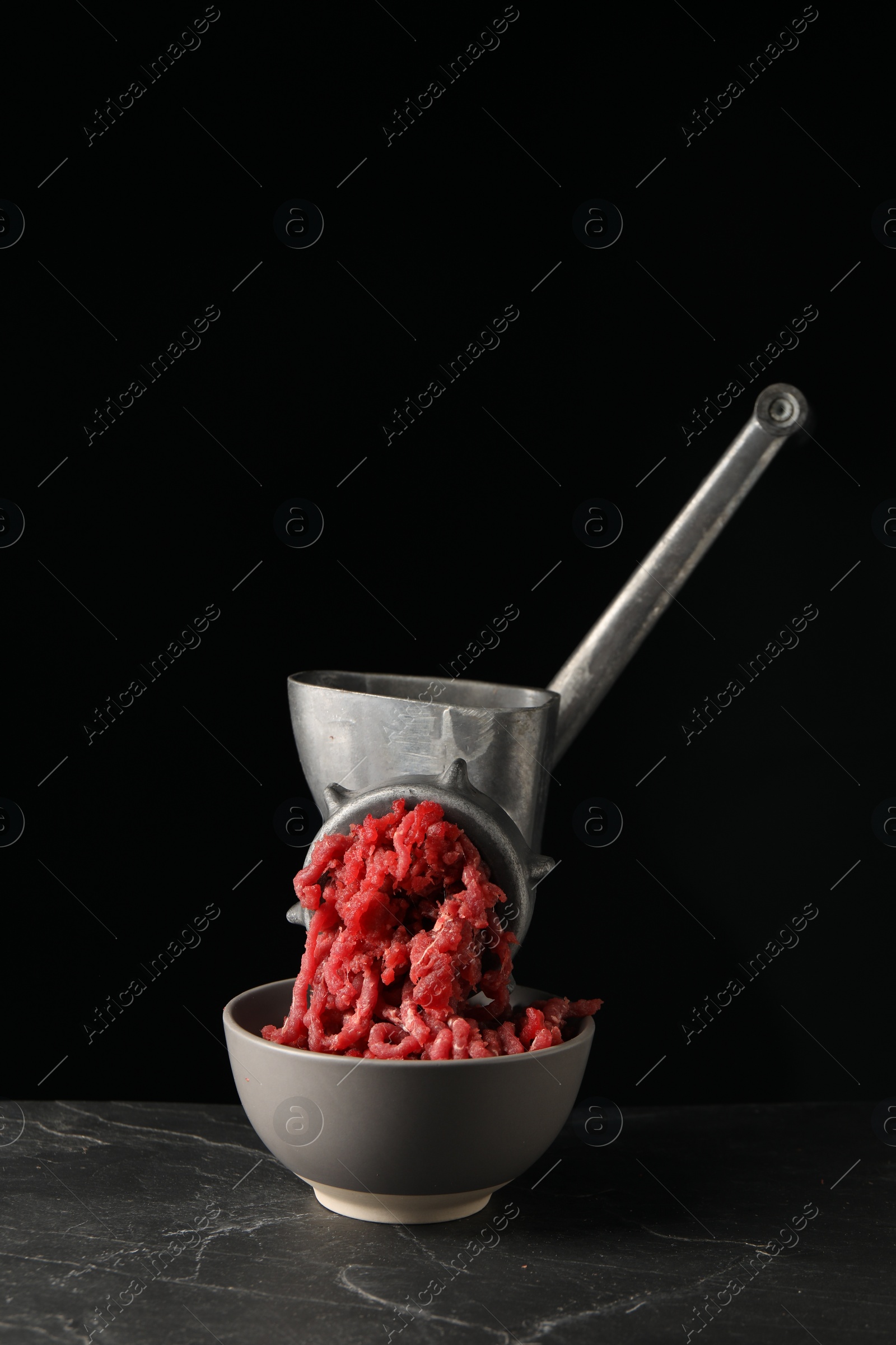 Photo of Metal meat grinder with beef mince on dark textured table against black background. Space for text