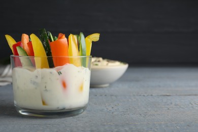 Photo of Fresh raw vegetable sticks with sauce on grey wooden table. Space for text