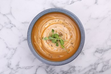 Delicious pumpkin soup with microgreens in bowl on white marble table, top view