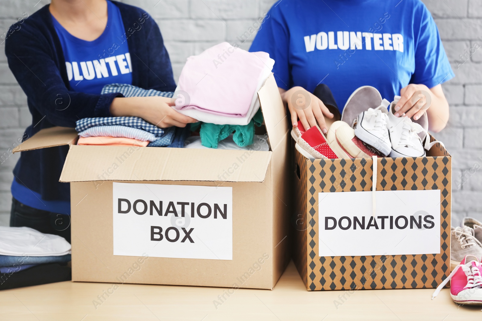 Photo of Female volunteers collecting clothes and shoes into donation boxes indoors