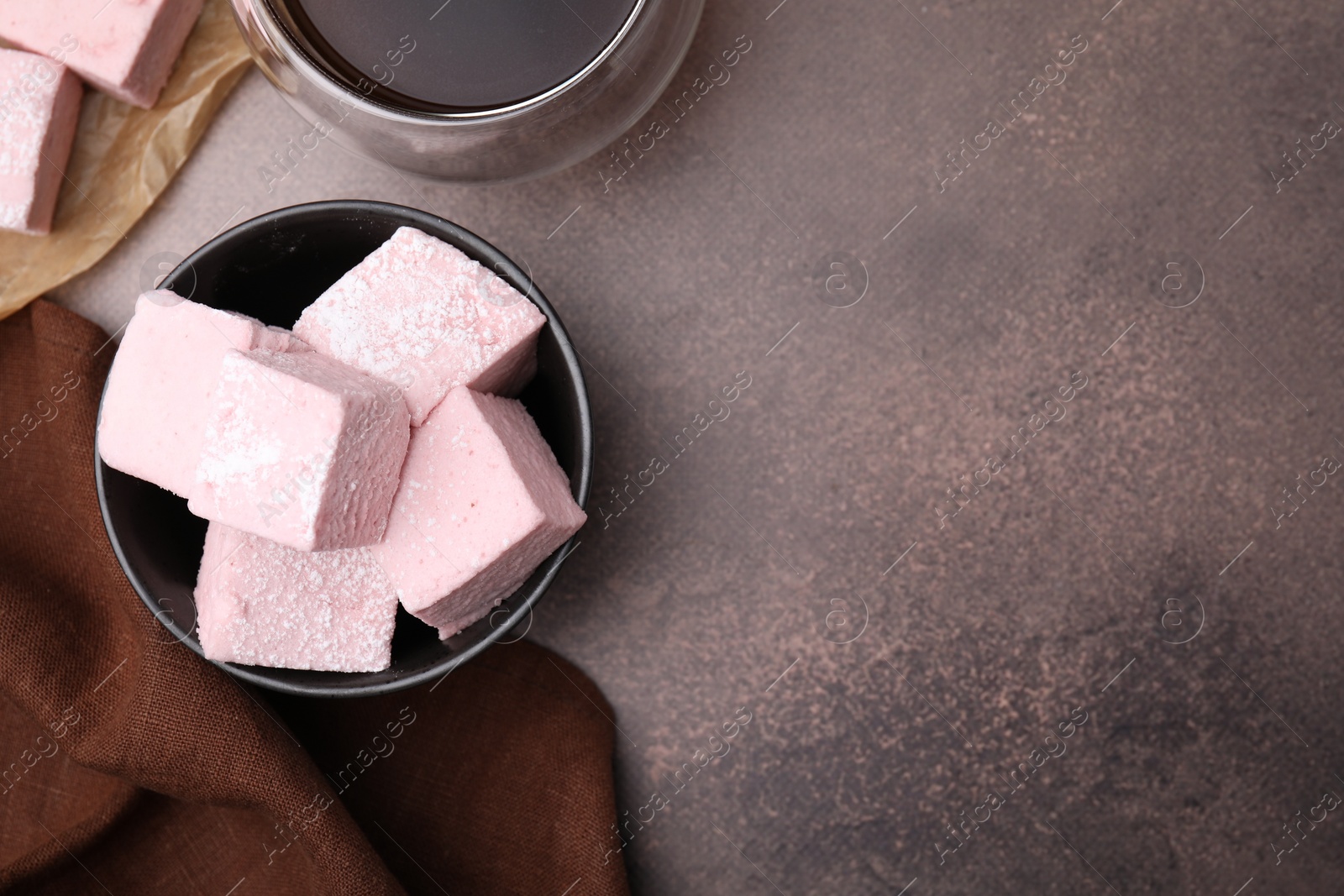 Photo of Bowl of delicious sweet marshmallows with powdered sugar on brown table, flat lay. Space for text