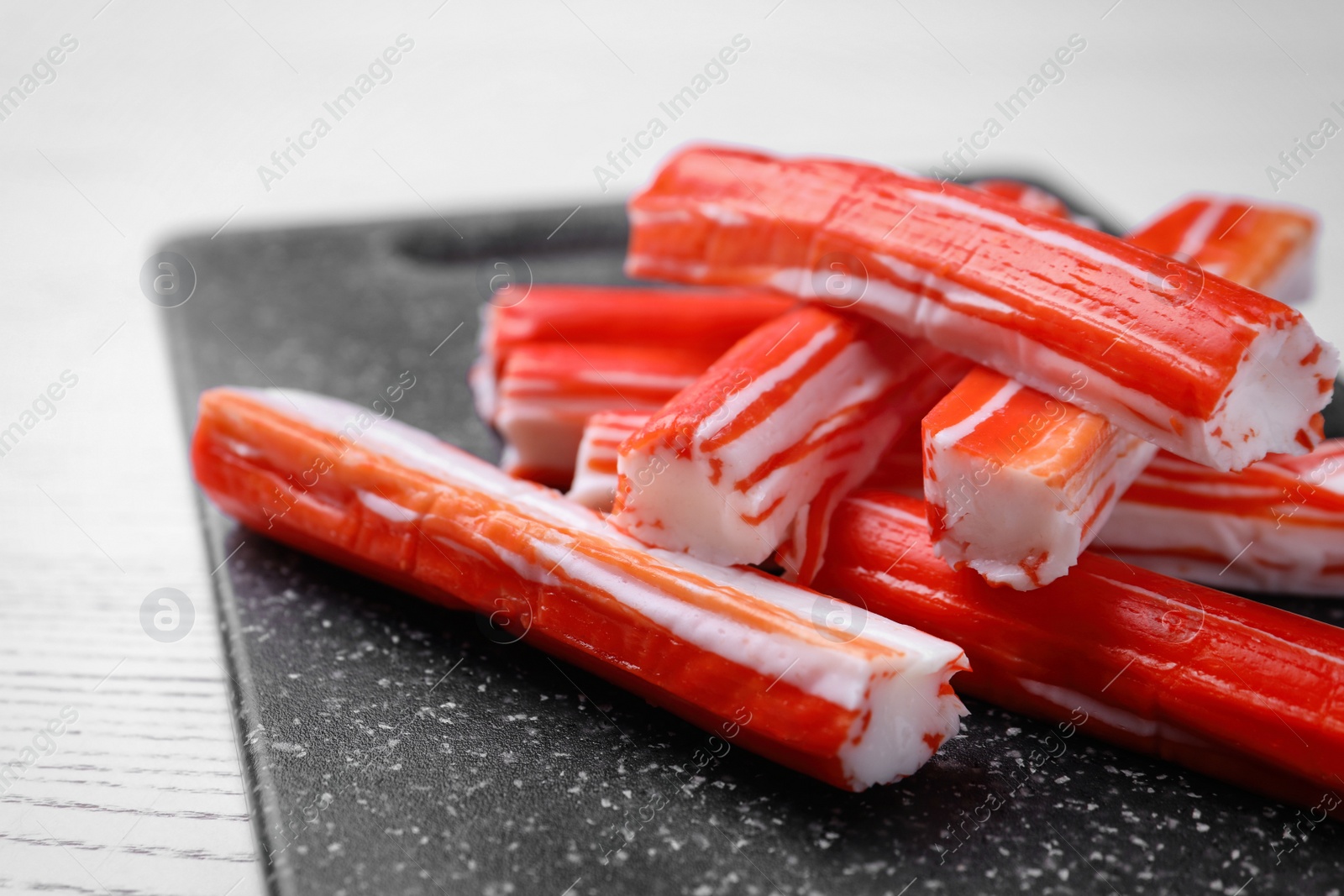 Photo of Delicious crab sticks on black board, closeup