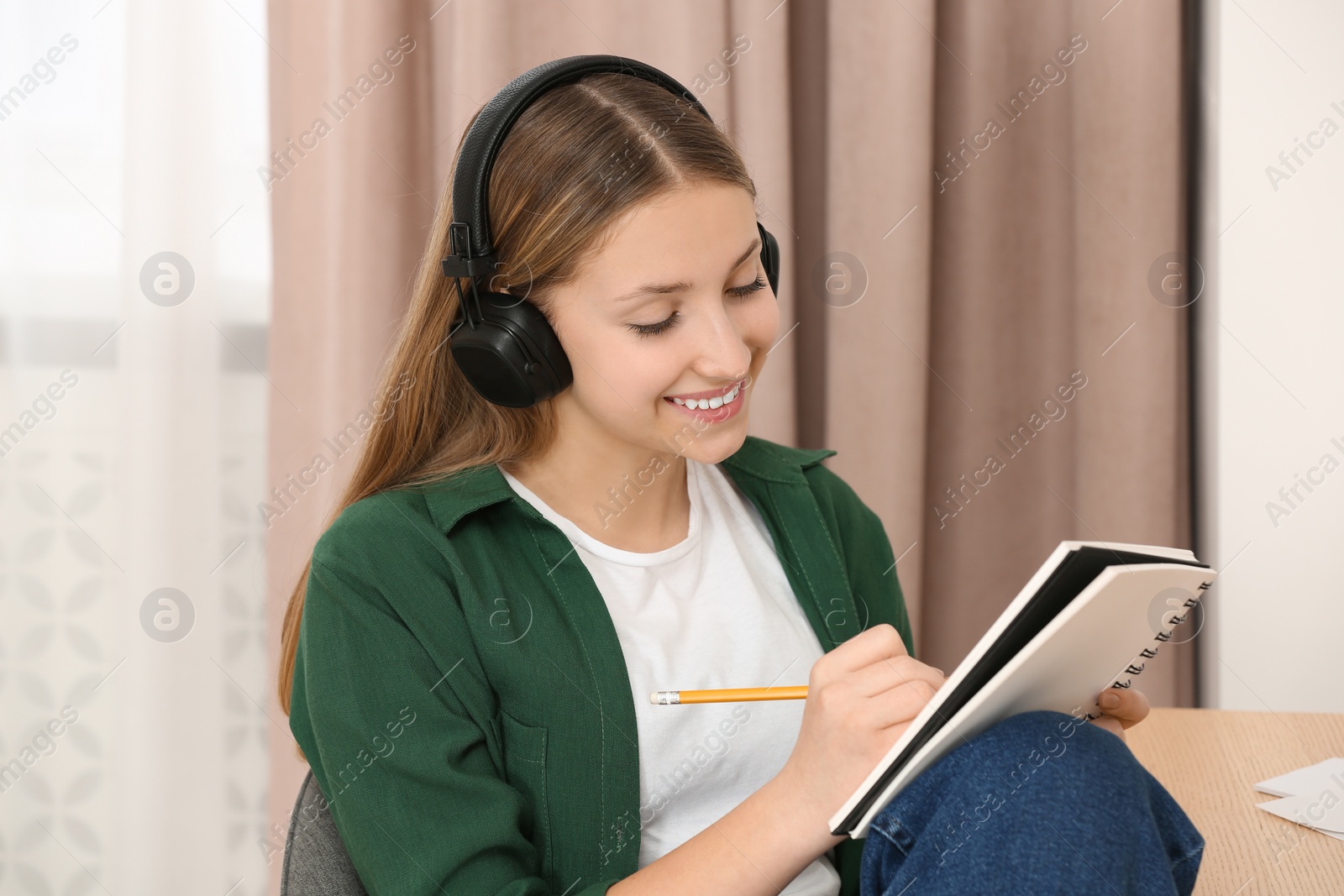 Photo of Teenage girl with headphones writing in notebook indoors