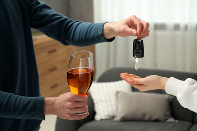 Man with glass of alcoholic drink giving car key to woman, closeup. Don't drink and drive concept